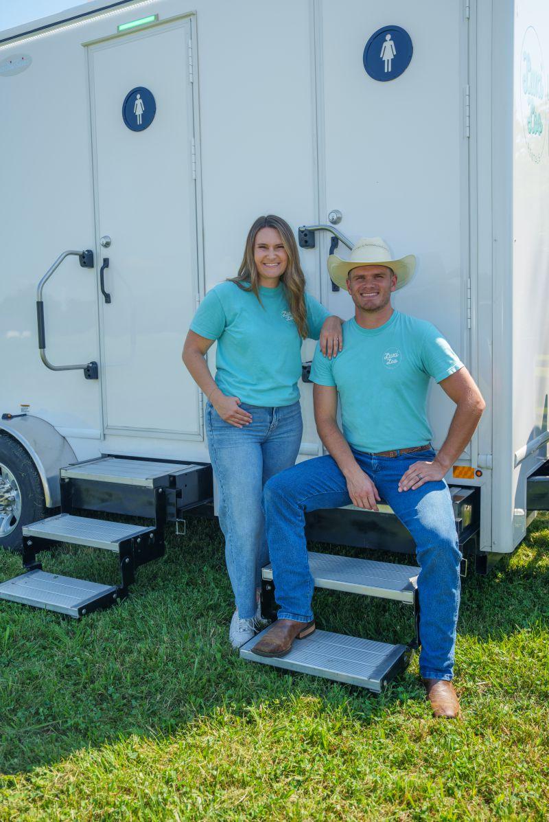 Justin and Rilee Campbell, owners of Luxi Loo Rentals in Bentonville, Arkansas, stand in front of a portable restroom trailer from Satellite Industries.